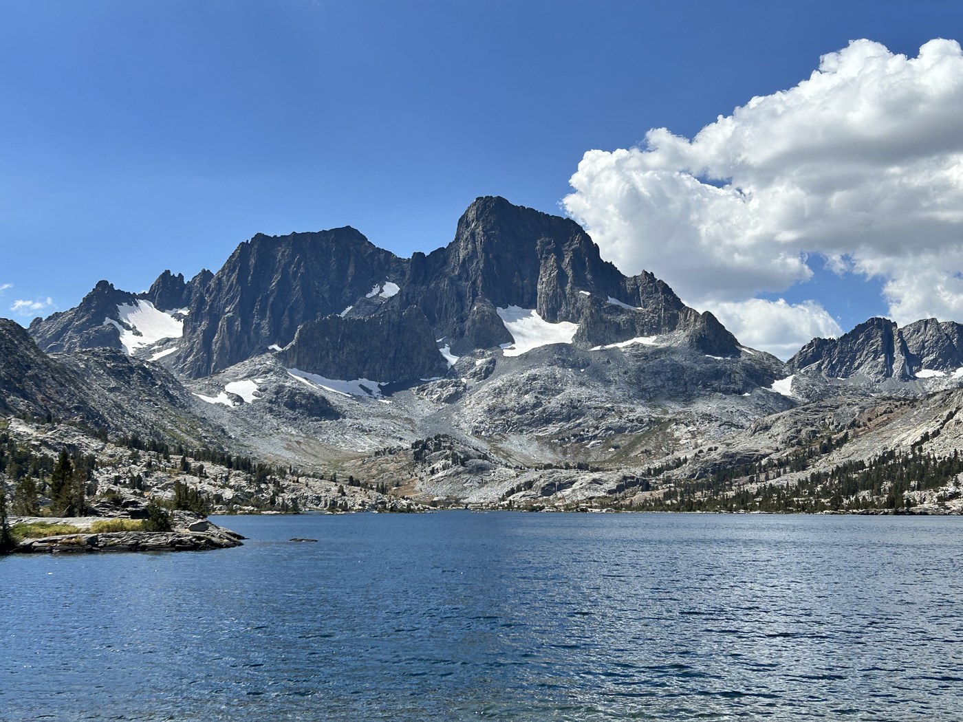 A large deep blue alpine lake with a broad dark peak and a small glacier standing at the far end under scattered cloud