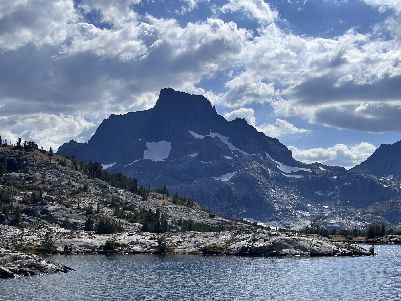 A wide alpine lake scattered with rocky islands, a dark pyramid-shaped peak rising at the head of the basin under a bright sky