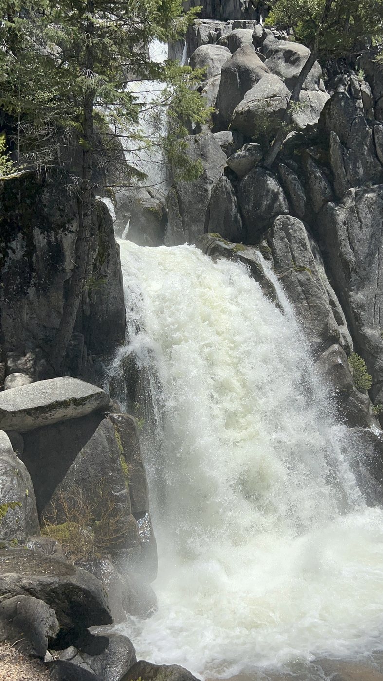 Close view of a large waterfall at full snowmelt flow pouring white over dark granite