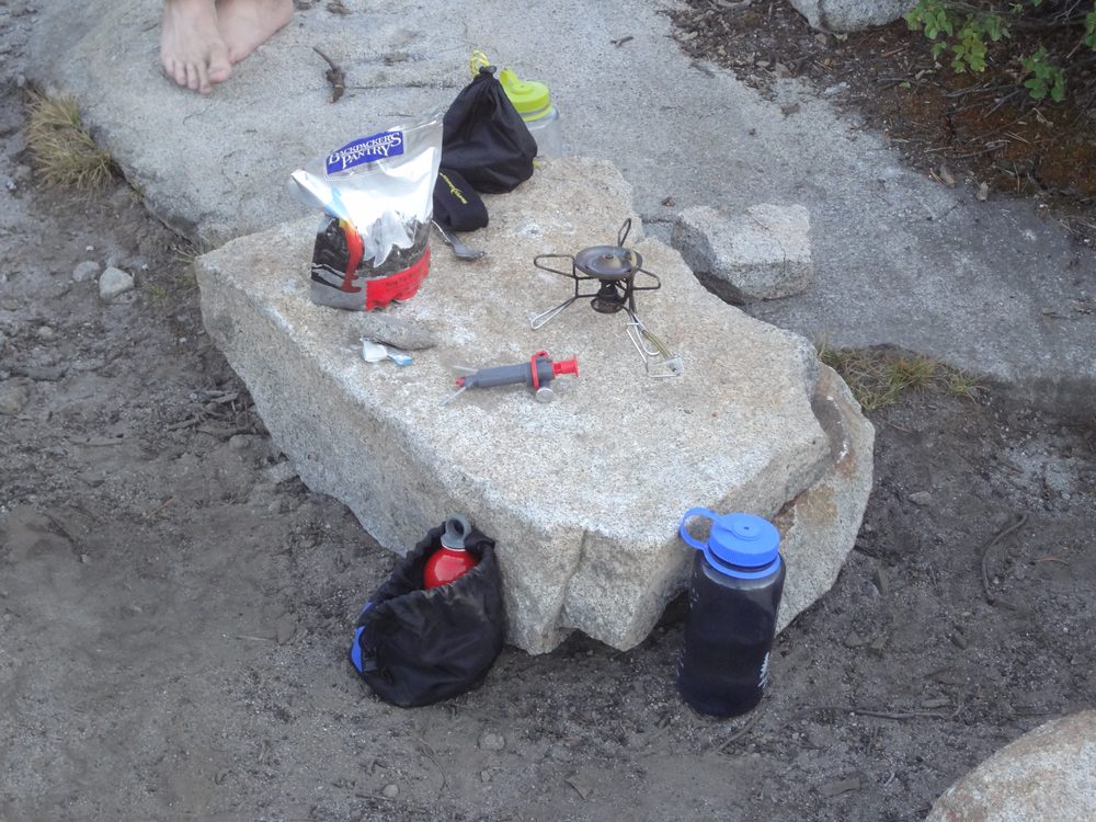 Beginner's camp kit spread on a granite boulder — borrowed stove, water filter, Snickers bag, Nalgene
