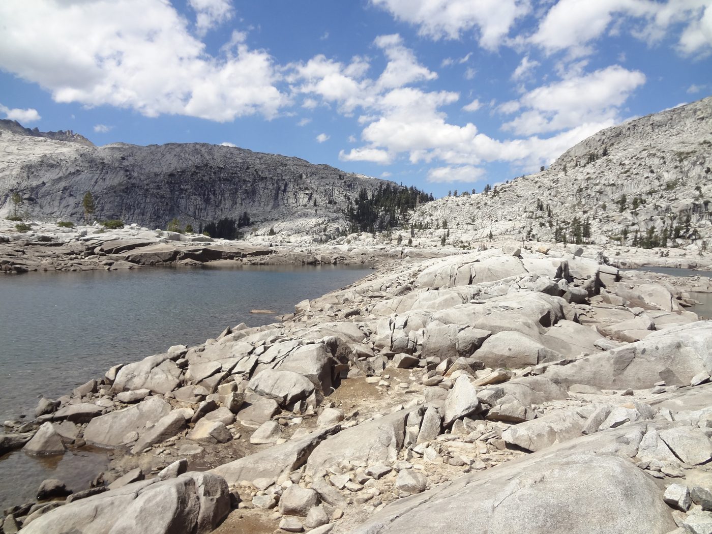 Wide view of an alpine lake in Desolation Wilderness with granite boulders and dramatic clouds