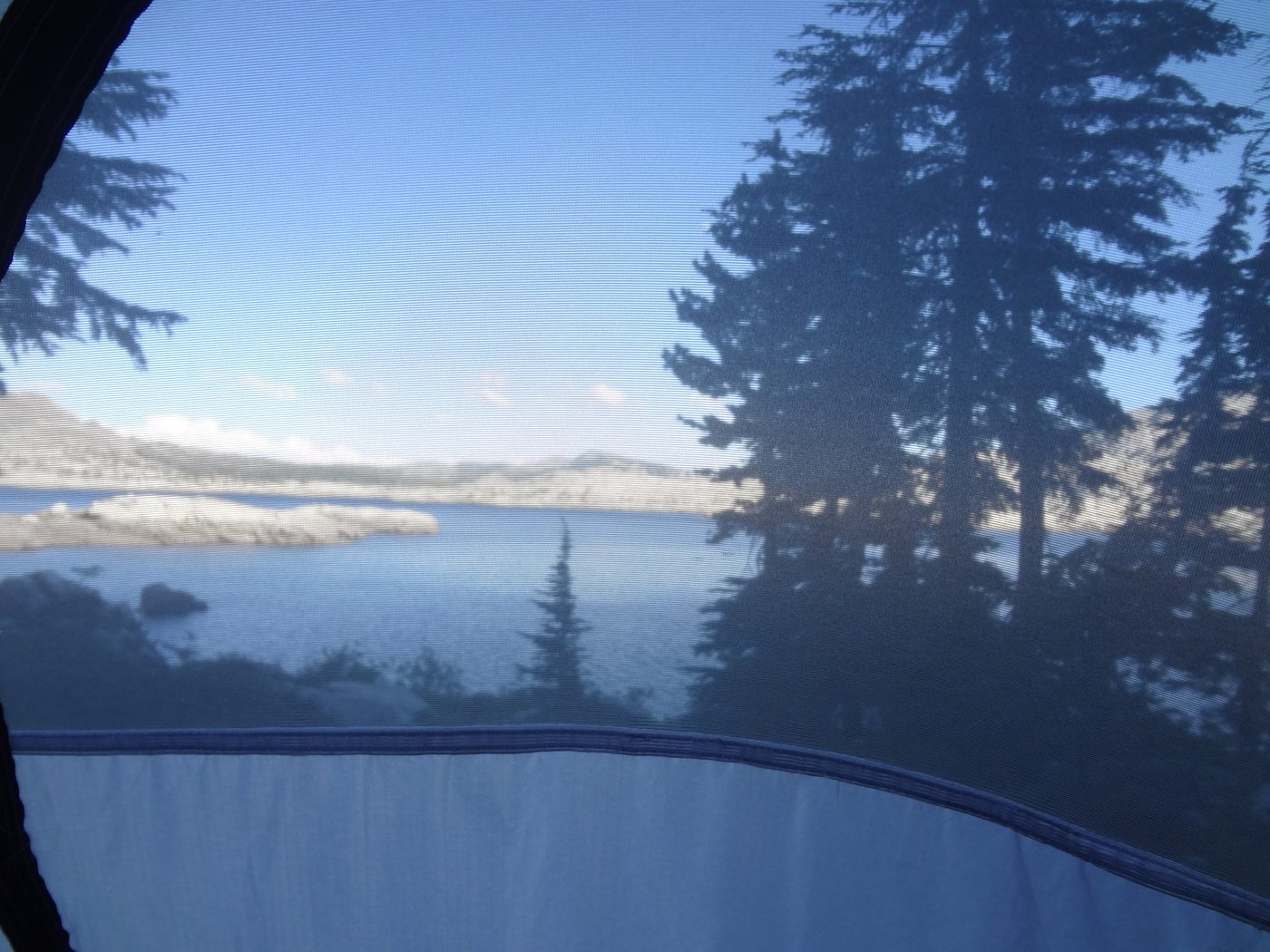 View of Desolation Wilderness alpine lake and ridgeline through a tent mesh door at dusk