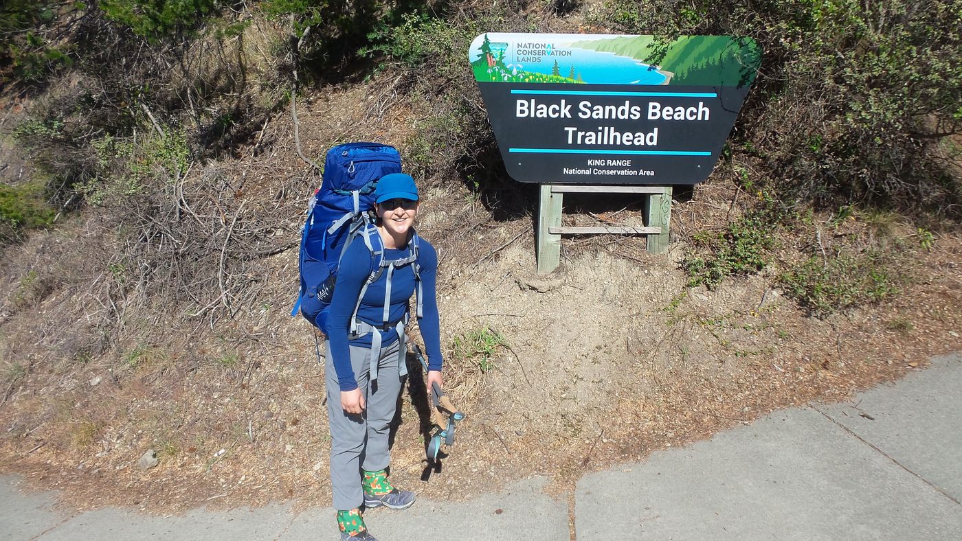 A backpacker at the Black Sands Beach Trailhead sign at the south end of the Lost Coast Trail