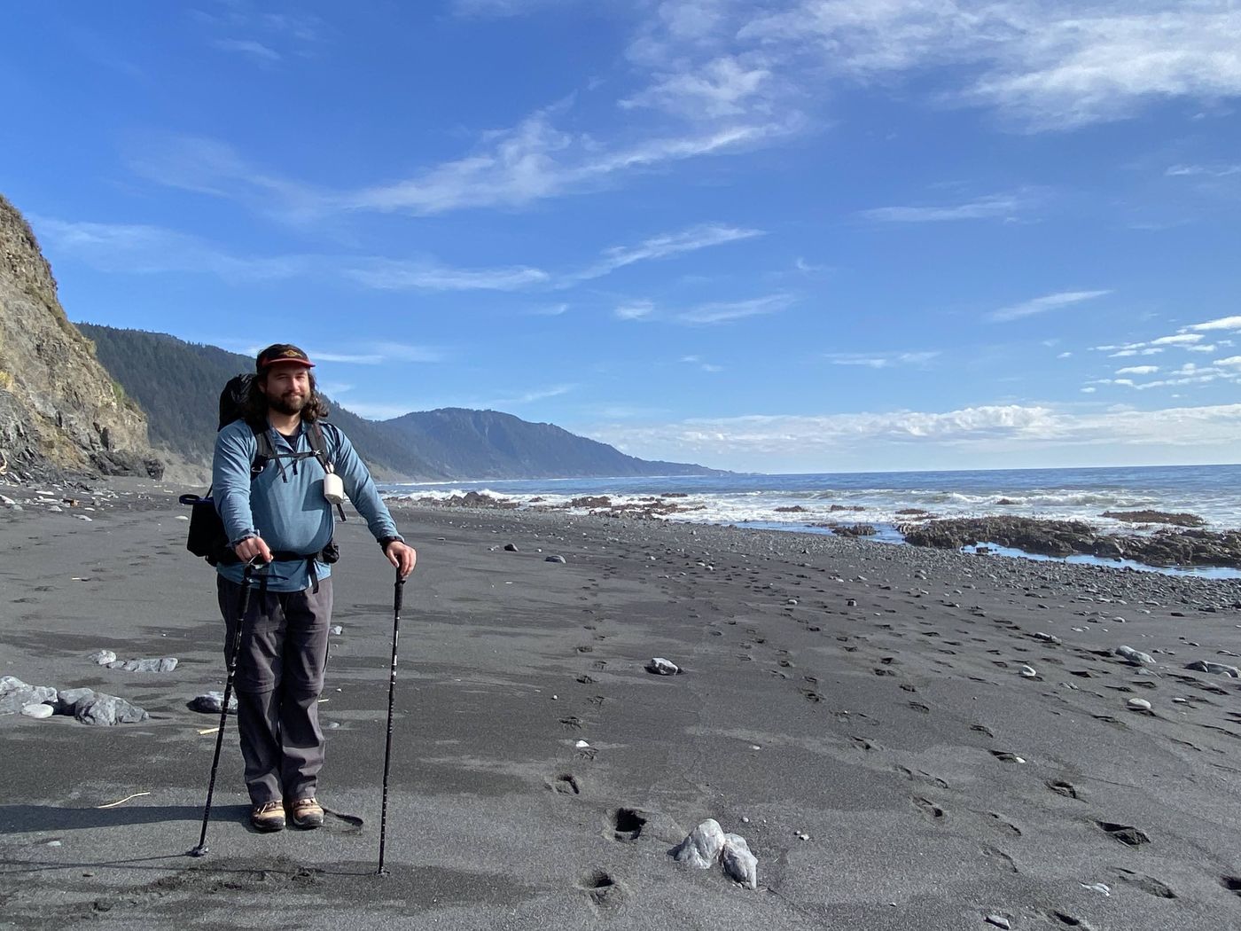 A backpacker on the black sand beach under clear blue sky with sea stacks on the Lost Coast