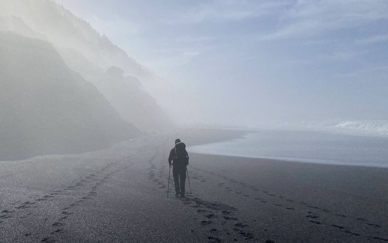 Hikers walking a foggy black-sand beach on the Lost Coast Trail