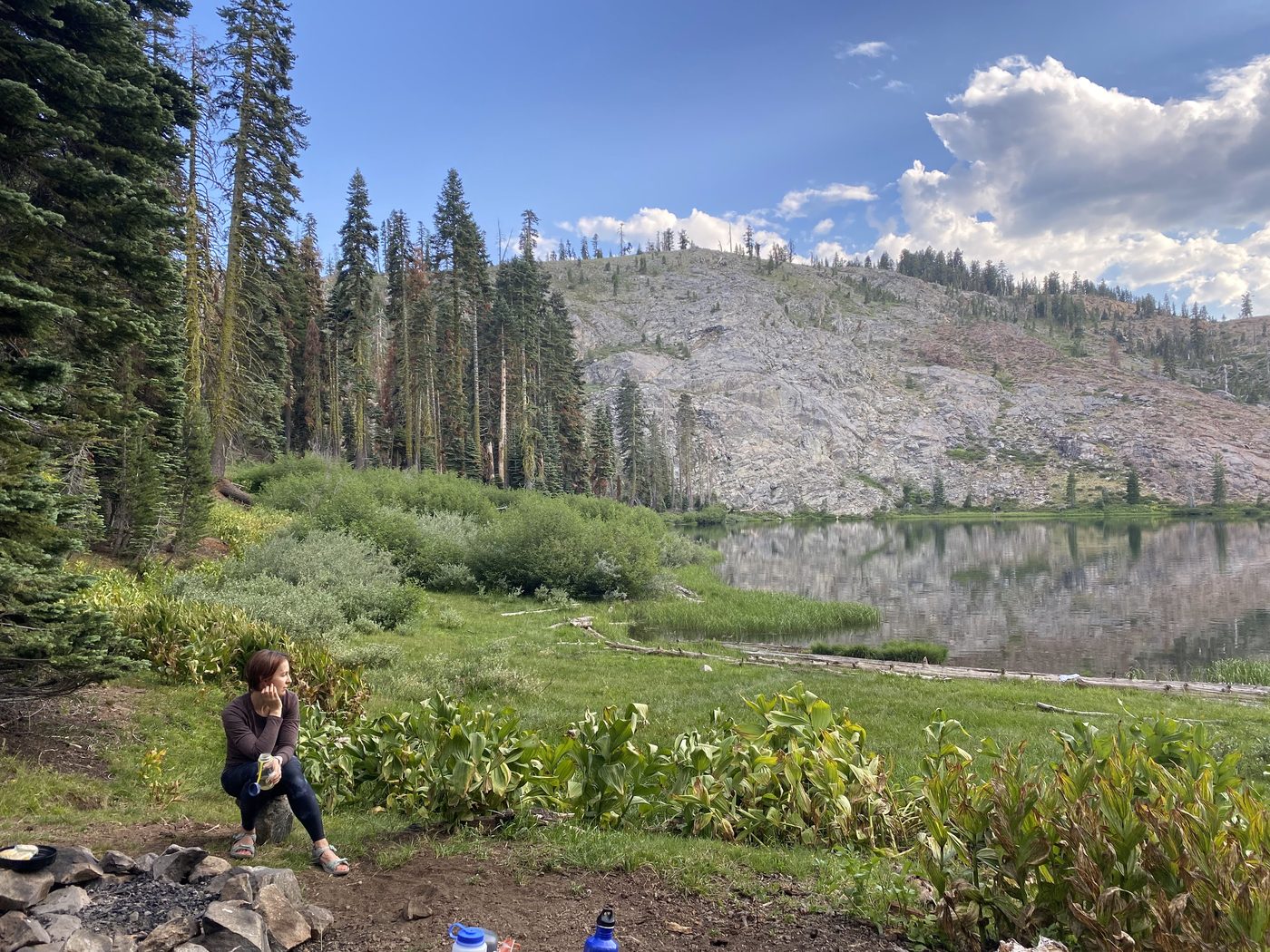 A woman sitting on a rock by the green shore of Milk Lake with a granite slope rising across the still water