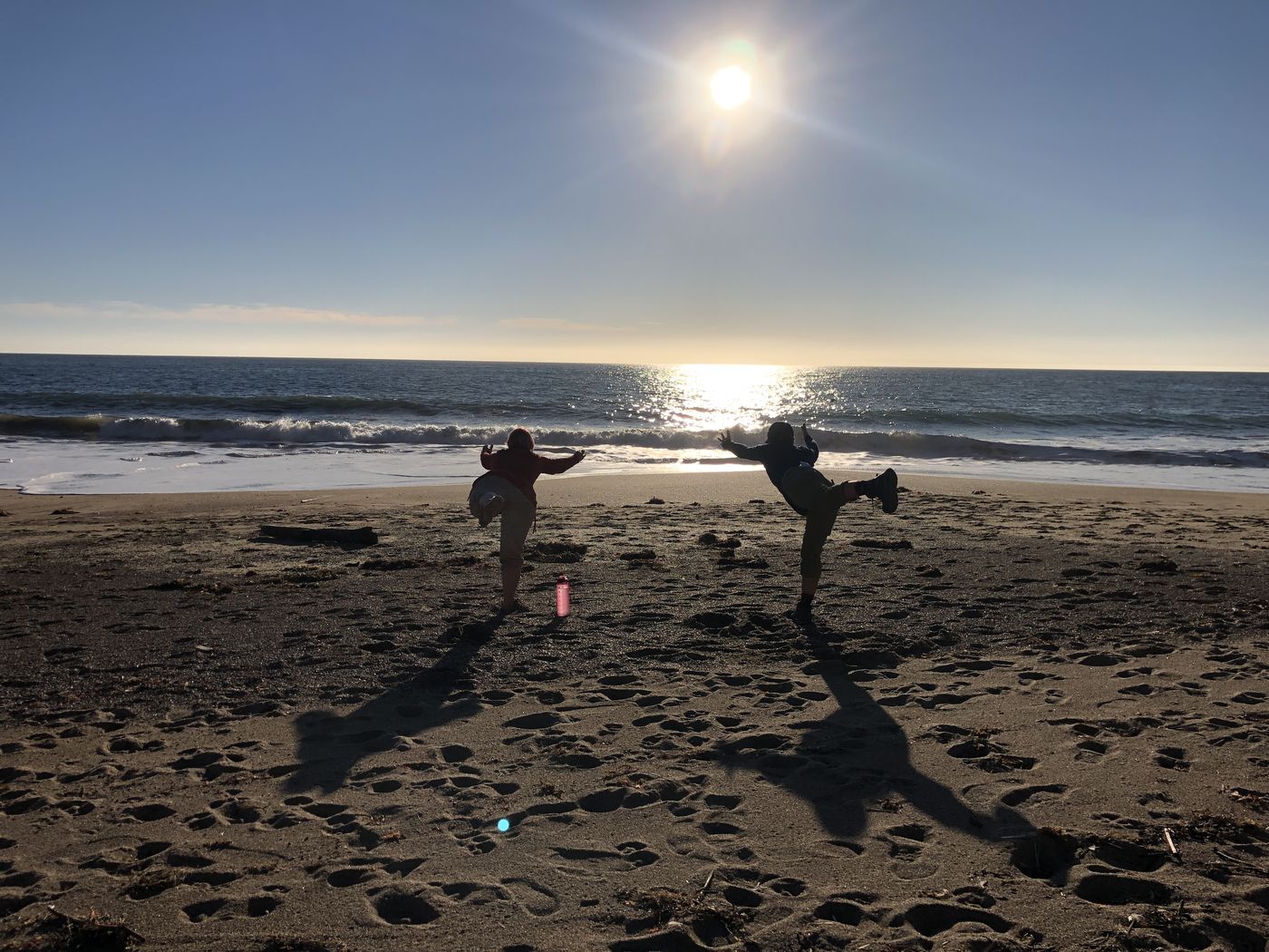 Two silhouetted figures goofing around on the beach against a low winter sun