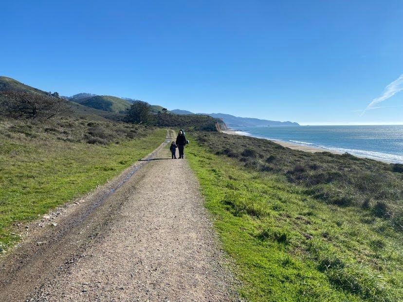 An adult and a small child walking a wide gravel road along the Point Reyes coast
