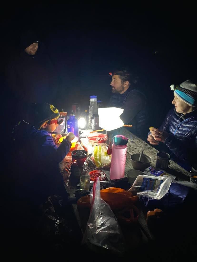 The group eating dinner by lantern light at a picnic table after dark