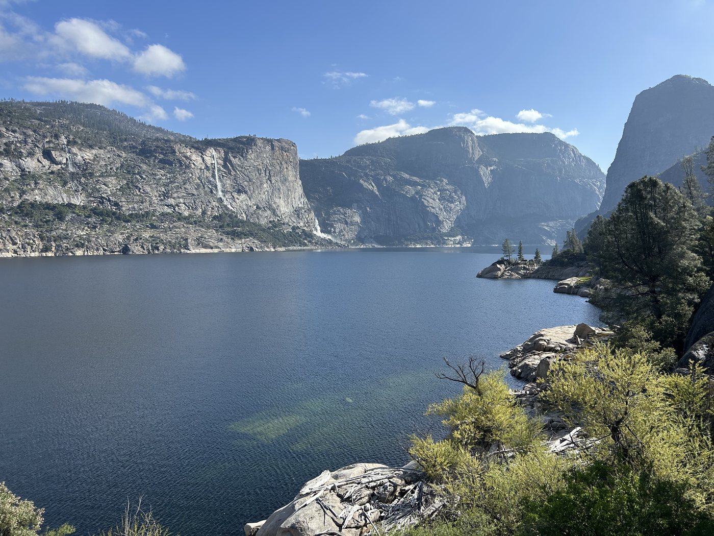 Hetch Hetchy Reservoir on a clear morning, deep blue water below high granite walls with waterfalls on the far side
