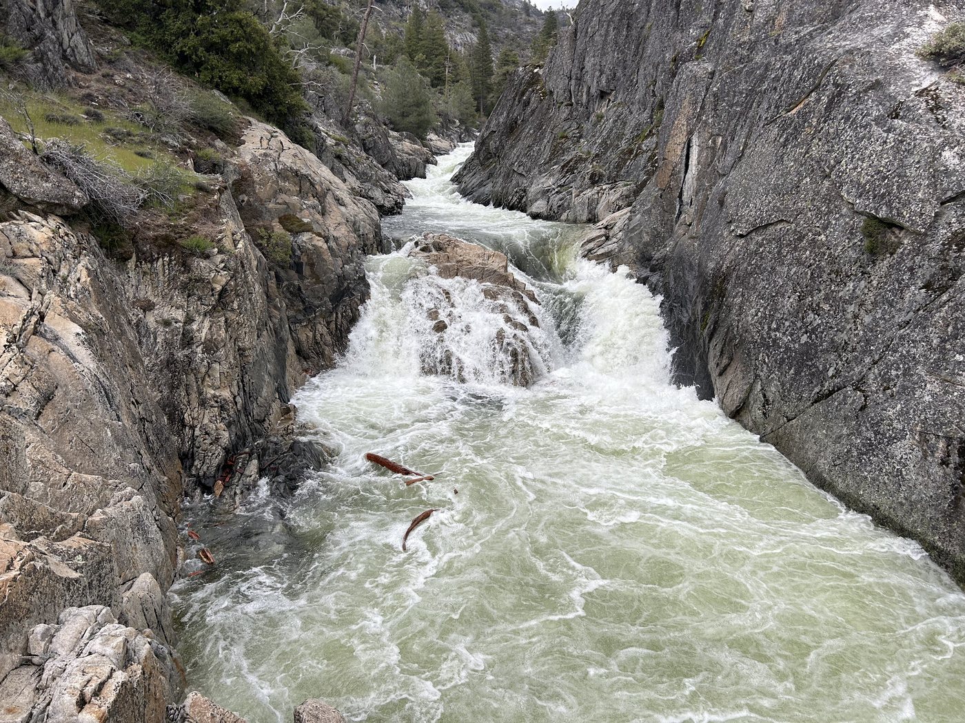 A steep granite gorge with pale green whitewater surging through it below the falls, dark cloud over the ridge beyond