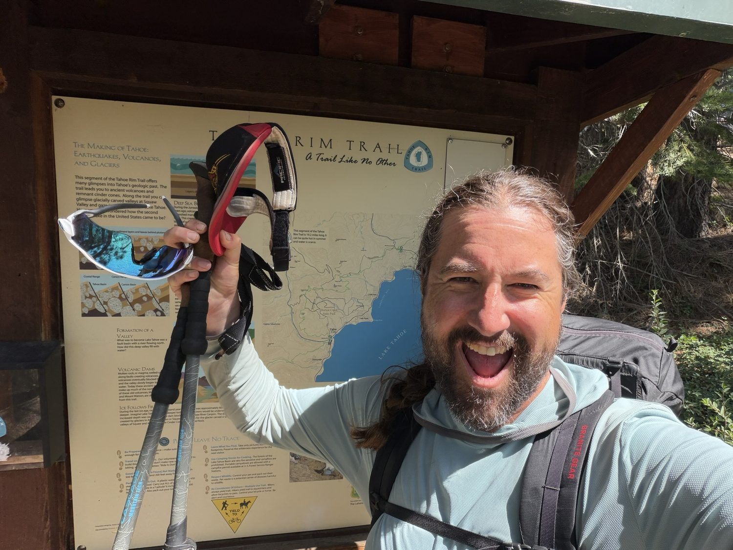 A jubilant hiker raising trekking poles in front of the Tahoe Rim Trail kiosk at Brockway Summit