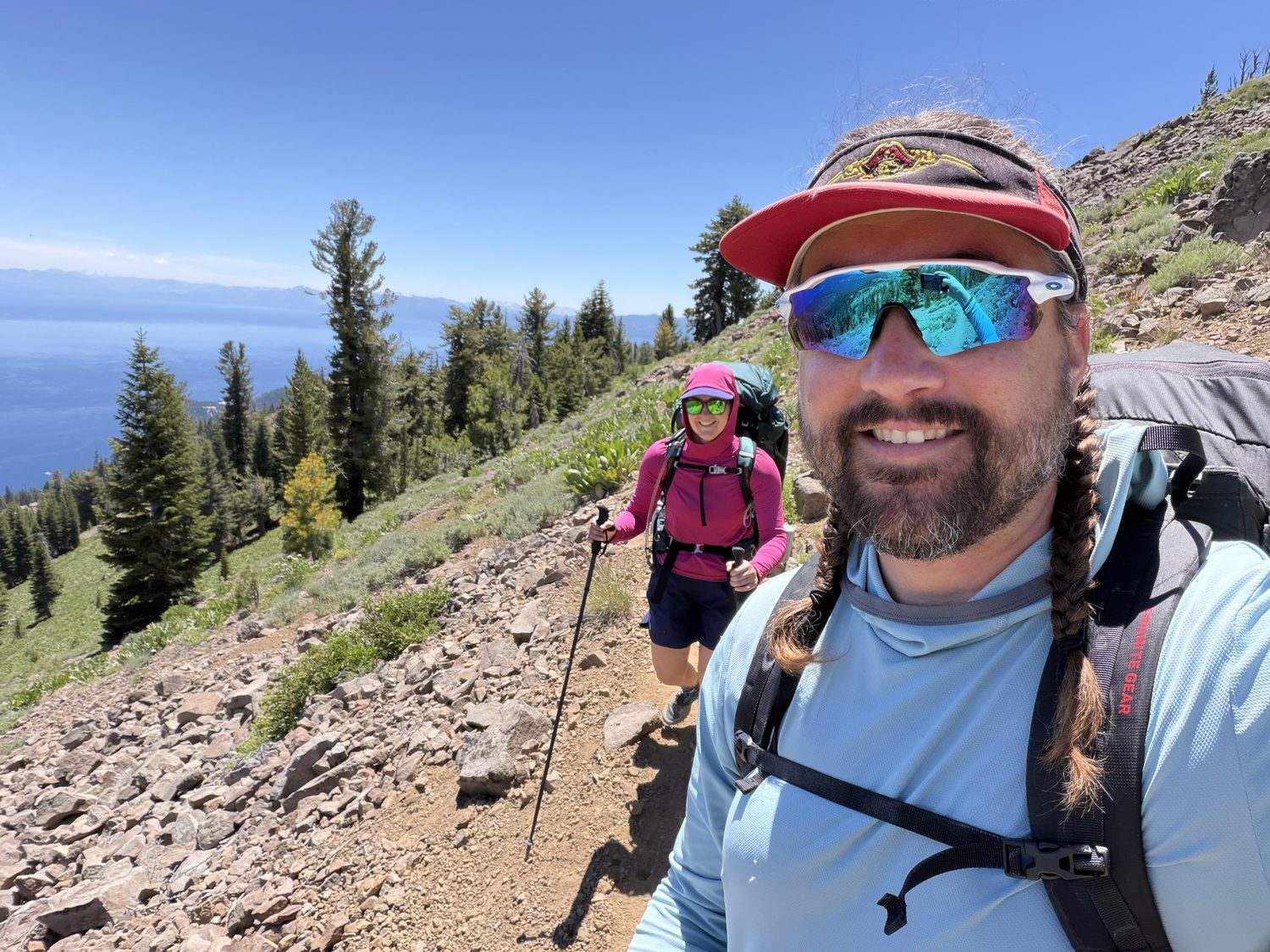 Two backpackers taking a selfie on an open sagebrush bench high above deep blue Lake Tahoe
