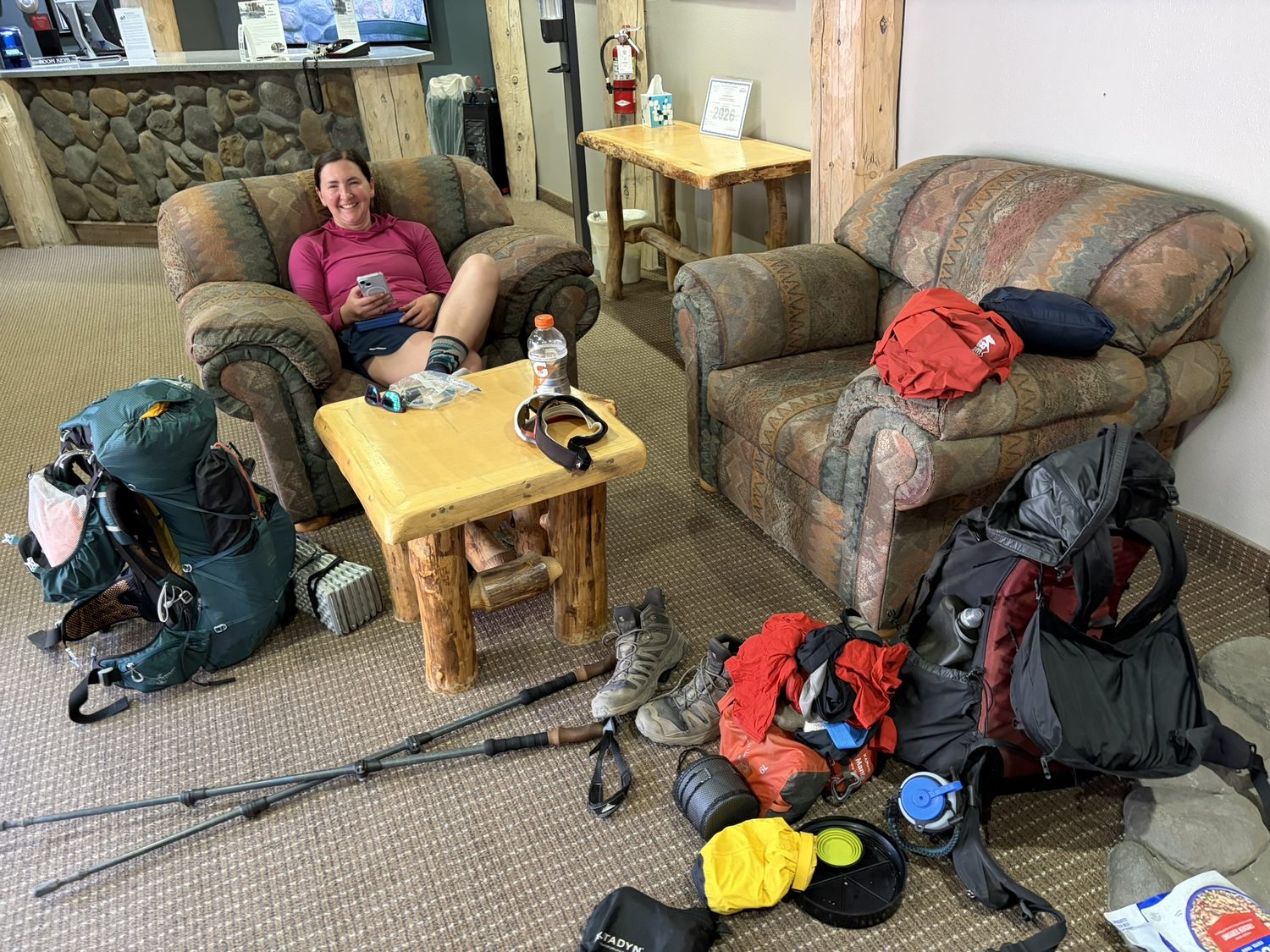 A hiker relaxing in a lodge armchair with backpacking gear scattered across the floor around her