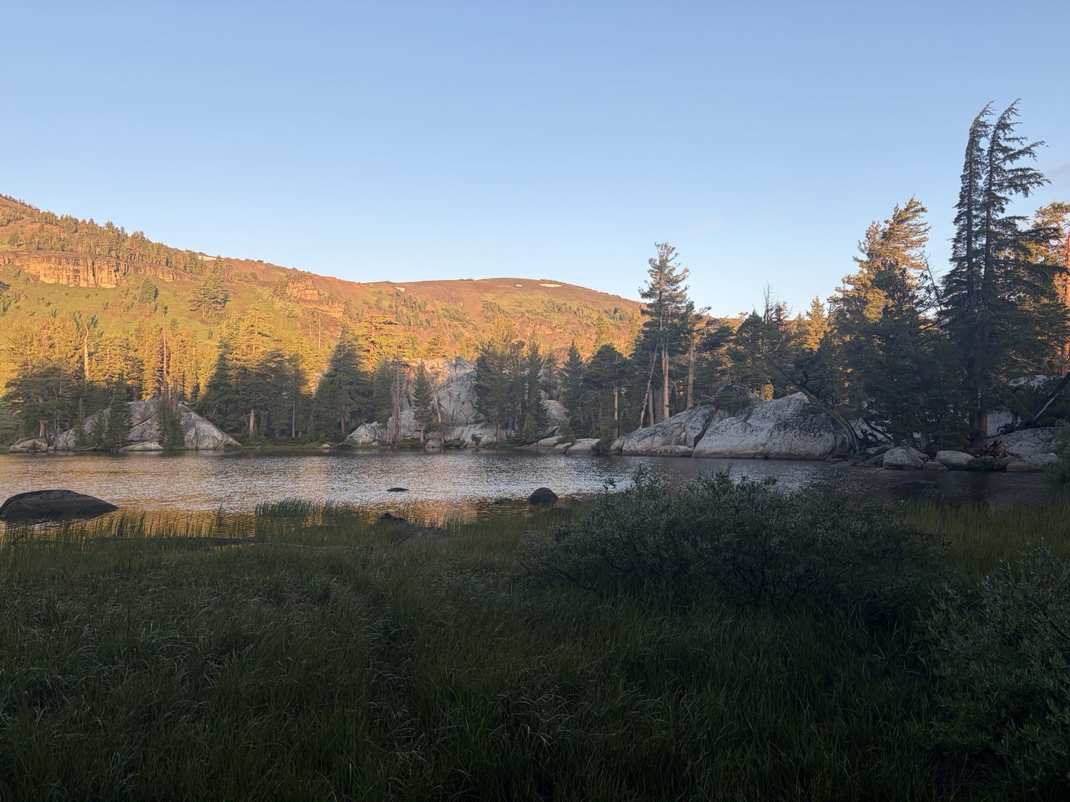 Golden sunrise light on a ridge above a calm alpine lake after the storm