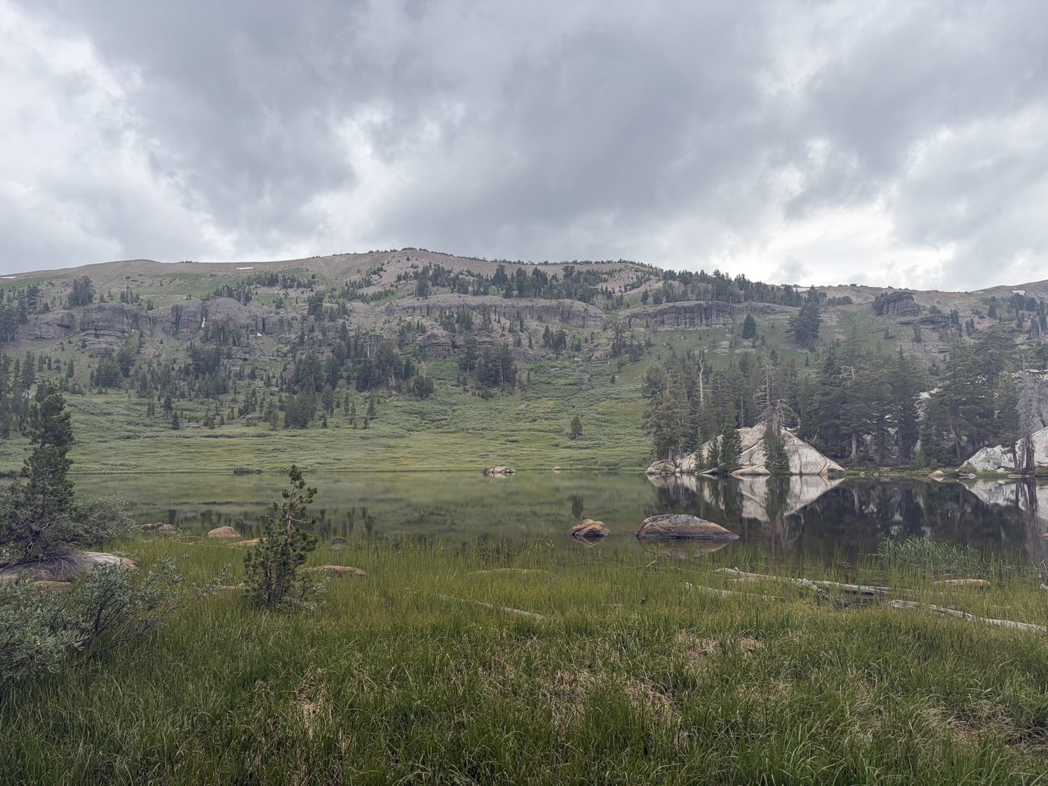 A still alpine lake reflecting heavy grey storm clouds at camp
