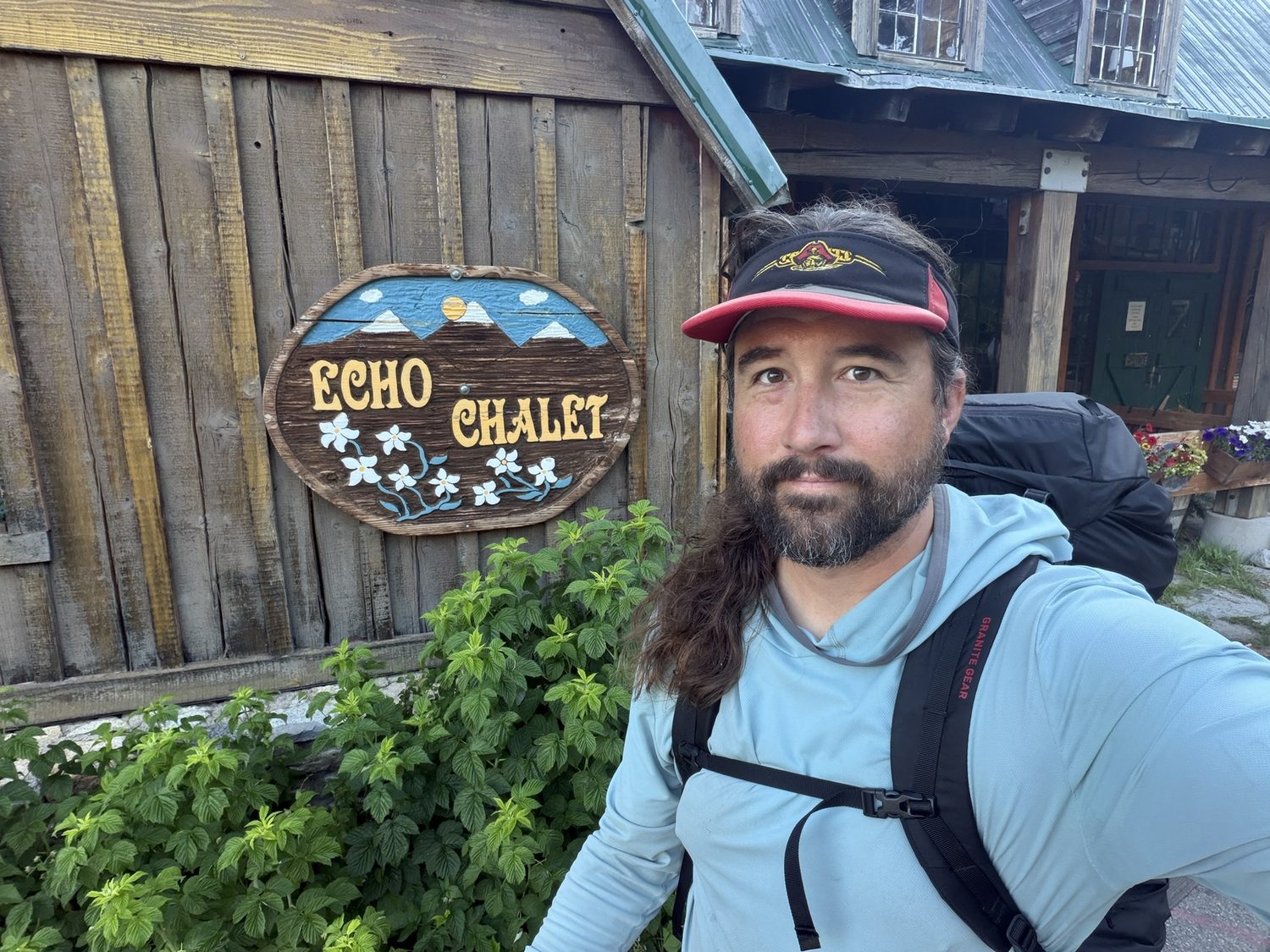 A hiker taking a selfie in front of the rustic Echo Chalet sign at Echo Lake