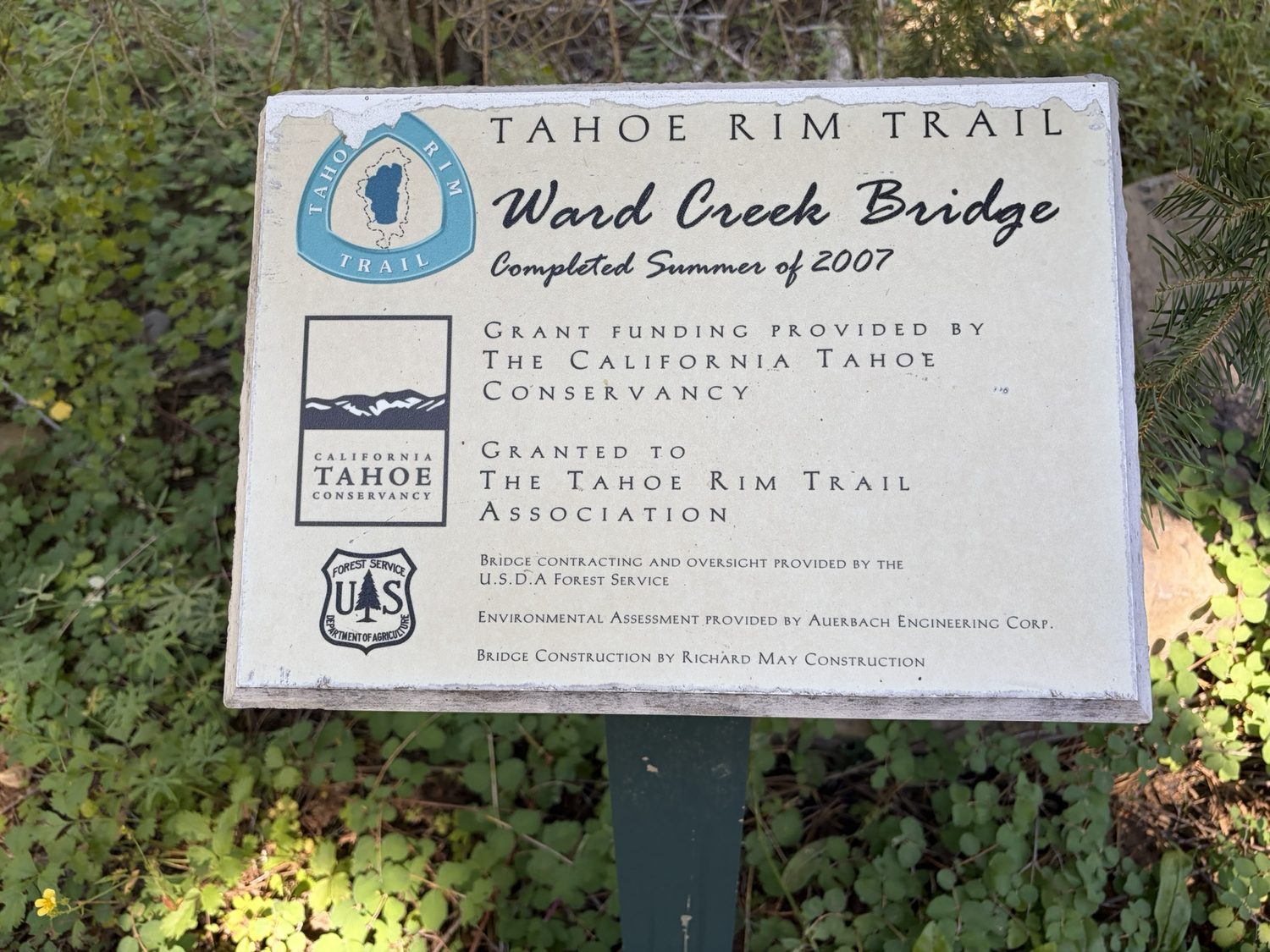 A Tahoe Rim Trail plaque for the Ward Creek Bridge beside a wooden trail bridge